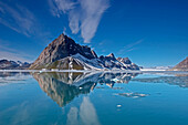 A jagged mountains casting a reflection into the melting fjord below.