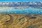 Luftaufnahme von gefaltetem metamorphem Gestein und Eisbergen im Sermilik Fjord.