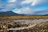 Glacial river flowing through the basalt landscape with a dramatic cloudy sky along the Kaldidalur Valley; Husafell, Nordurland Vestra, Iceland