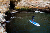 A stand up paddleboarder on the rough coastline north of Santa Cruz.