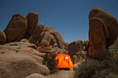An illuminated tent beneath granite rocks and Orion's Belt.