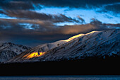 Sunset light breaks through the clouds and lights up a mountain.