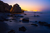 Rock formations along El Matador State Beach at night with the city lights of Los Angeles in the background; Malibu, California, United States of America