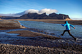 Ein Mann springt über einen Bach an der Südküste von Island.