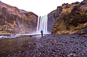 Ein Mann geht zum Wasserfall Skogafoss in Island.