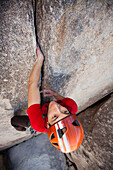 A trad climber ascends a shallow crack on a vertical granite wall.
