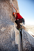 A climber balances his body to reach a higher hold.