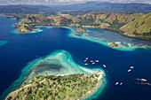 Aerial view of boats moored along the shore of an island in the Komodo National Park, home of the famous Komodo Dragon; East Nusa Tenggara, Lesser Sunda Islands, Indonesia