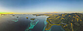 Luftaufnahme der Komodo-Inseln mit leuchtend gelbem Sonnenlicht am Horizont, Komodo-Nationalpark, Heimat des berühmten Komodo-Drachen; Ost-Nusa Tenggara, Kleine Sunda-Inseln, Indonesien