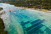 Aerial of boats on the waterway passing under the iconic Yellow Bridge connecting Nusa Lembongan and Nusa Ceningan, also showing the underwater patches of seaweed farming through the shallow, turquoise water; Klungkung Regency, East Bali, Bali, Indonesia