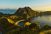 Travelers on hilltop watching the sunset with boats moored in the bay at Padar Island in Komodo National Park in the Komodo Archipelago; East Nusa Tenggara, Indonesia
