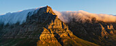 Blick vom Lion's Head auf den sonnenbeschienenen Tafelberg mit einer Wolkenformation, die einen Tischtuch-Effekt über den Bergspitzen erzeugt; Kapstadt, Westkap-Provinz, Südafrika