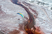 Ein Motorschirmpilot fliegt über den Owens Lake, einem größtenteils trockenen Seebett, in der Sierra Nevada bei Lone Pine, wo salzliebende Halobakterien das flache Wasser durch die salzigen Rückstände rot färben; Lone Pine, Inyo County, Kalifornien, Vereinigte Staaten von Amerika