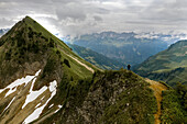 Ein Wanderer erreicht einen Berggipfel und blickt auf die herrliche Aussicht auf die Alpen bei bewölktem Himmel; Feldkirch, Vorarlberg, Österreich