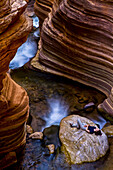 A hiker relaxing on a large rock in a slot canyon at the Colorado River Mile 136 in the Arizona Cascades along Deer Creek; Grand Canyon National Park, Arizona, United States of America