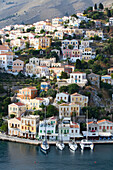 Überblick über pastellfarbene Gebäude und Segelboote entlang der Uferpromenade am Hafen von Gialos, Insel Symi (Simi); Dodekanes-Inselgruppe, Griechenland