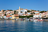 Traditional buildings and boats moored along the waterfront in the harbor at Emborio, the main town on Halki (Chalki) Island; Dodecanese Island Group, Greece