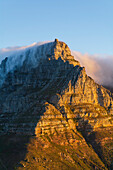 Ein Blick auf den sonnenbeschienenen Tafelberg vom Lion's Head mit einer Wolkenformation, die einen Tischtuch-Effekt über den Berggipfeln erzeugt; Kapstadt, Provinz Westkap, Südafrika