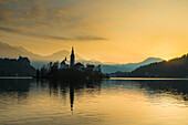 Silhouette der Kirche und anderer Gebäude am Bleder See in der Morgendämmerung; Bled, Slowenien