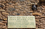 Plaque on fortress wall stating Emperor Birhan Seghed Kuregna, (Birhan Seghed Kuregna Iyasu Anditegie Mintiwab's Castle) time of rule with a bird perched in an embrasure at the Fasil Ghebbi fortress located in Gondar, Amhara Region; Ethiopia
