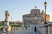 View of the Castel Sant'Angelo (Mausoleum of Hadrian) with a pedestrian and a Nun crossing the Ponte Sant'Angelo; Rome, Lazio, Italy