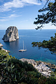 Blick auf die Faraglioni-Bucht und Felsformationen mit einem Segelboot, das am Ufer in der Bucht von Neapel vor der Insel Capri vertäut ist; Neapel, Capri, Italien