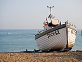 Wooden fishing boat beached along the shore of the pebble beach with sea in background; Hastings, East Sussex, England, United Kingdom