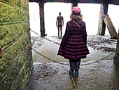 View taken from behind of a woman posing as Antony Gormley's cast iron figure, Another Time 1999-2013, looking out at the sea from the Folkestone Harbour Arm; Folkestone, Kent, England, United Kingdom