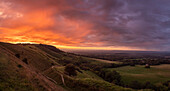 The sun sets over England's South Downs National Park, lighting up the rainfall like fire; Ditchling, East Sussex, England