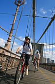 Paar fährt mit dem Fahrrad über die Brooklyn Bridge in New York City; Brooklyn Bridge, New York.