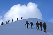 Eine Gruppe von Skifahrern, die eine verschneite Piste hinauffahren; Selkirk Mountains, British Columbia, Kanada.