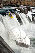 Winterlicher Wildwasserkajakfahrer am Rande eines großen Wasserfalls mit Eis; Great Falls, Potomac River, Maryland.