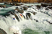 Zwei Wildwasserkajakfahrer paddeln gemeinsam über fast zugefrorene Wasserfälle; Great Falls, Potomac River, Maryland.