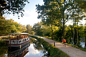 Ein Radfahrer fährt auf dem C & O Kanal an einem Lastkahn vorbei; C&O Canal Towpath, Great Falls, Maryland.