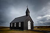 Die Schwarze Kirche von Budir in der Küstenlandschaft mit einem stürmischen Himmel; Budakirkja, Island
