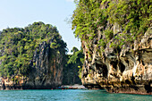 Blick auf die Felsformationen und Klippen entlang des Ufers einer kleinen Bucht mit am Strand vertäuten Booten auf einer tropischen Insel; Phang Nga Bay, Thailand