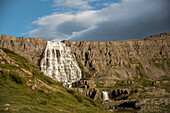 Der Dynjandi-Wasserfall mit einer dunklen Wolkenformation über den sonnenbeschienenen Klippen ist der Hauptwasserfall von Dynjandi, einer Reihe von 7 Wasserfällen im Arnarfj?r und den größten Wasserfällen in den Westfjorden von Island; Arnarfjordur, Westfjorde, Island