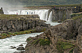 People viewing the gushing water of the Goðafoss Waterfall. Godafoss is in Northern Iceland about 45 minutes from Akureyri, Iceland's second largest city. The water, from the river Skjálfandafljót falls from a height of 36 feet; North Central Region, Iceland