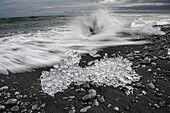 Wellen brechen an den schwarzen Sandstrand von Jokulsarlon, der Gletscherflusslagune, wo das Eis des Vatnajokull-Gletschers in die Lagune fällt und dort bleibt, bis es klein genug ist, um ins Meer zu treiben. Der Vatnajokull ist der größte Gletscher in Island; Djupivogur, Südküste, Island