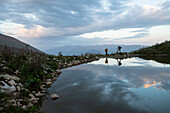 Adventure exploration expedition as two explorers stop for a rest next to a small lake on their way to a base camp close to Veryovkina, cave entrance high in the Caucasus Mountains; Gagra, Caucasus Mountains, Abkhazia