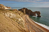 People walking along the beach with views of the Atlantic Ocean and Durdle Door rock formation on the Jurassic Coast near Lulworth; Dorset, England, Great Britain
