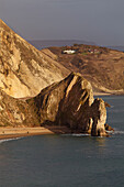 People walking along the beach around Durdle Door overlooking the Atlantic Ocean on the Jurassic Coast World Heritage Site near Lulworth Cove with houses hidden in the cliff tops; Dorset, England, Great Britain