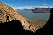 The shadow of expedition team member climbing the cliffs searching for more caves with lake Centrum in the background.