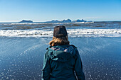 Rückenansicht einer Frau, die an der Südküste Islands steht und auf die Westmännerinseln hinausschaut; Hella, Südküste, Island