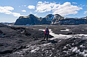 Frau steht auf einem Gletscher und schaut auf die bergige Landschaft an der Südküste Islands; Vik, Südisland, Island