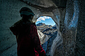 View through an ice cave of a woman exploring a glacier while traveling in Iceland; Vik, South Iceland, Iceland