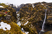 Distant view of a woman standing and overlooking Mulagljufur Canyon, a hikers paradise, with an amazing view of the waterfalls, river and moss-covered cliffs; Vik, South Iceland, Iceland