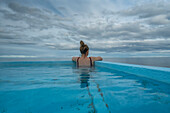 Blick von hinten auf eine Frau, die in einem heißen Pool an der Nordküste Islands sitzt und auf den Atlantik hinausschaut; Djupavik, Strandir Küste, Island