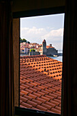 Ziegeldach und der Eingang zum Hafen durch ein Fenster; Collioure, Pyrenees Orientales, Frankreich