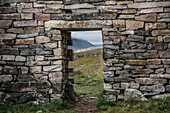 Close-up of a stone wall with an opening looking through to a scenic view at the archaeological site of Hvalsey, near Qaqortoq, where there is an ancient ruin of a church dating to 1300 AD at the Southern tip of Greenland in the North Atlantic; Southern Greenland, Greenland
